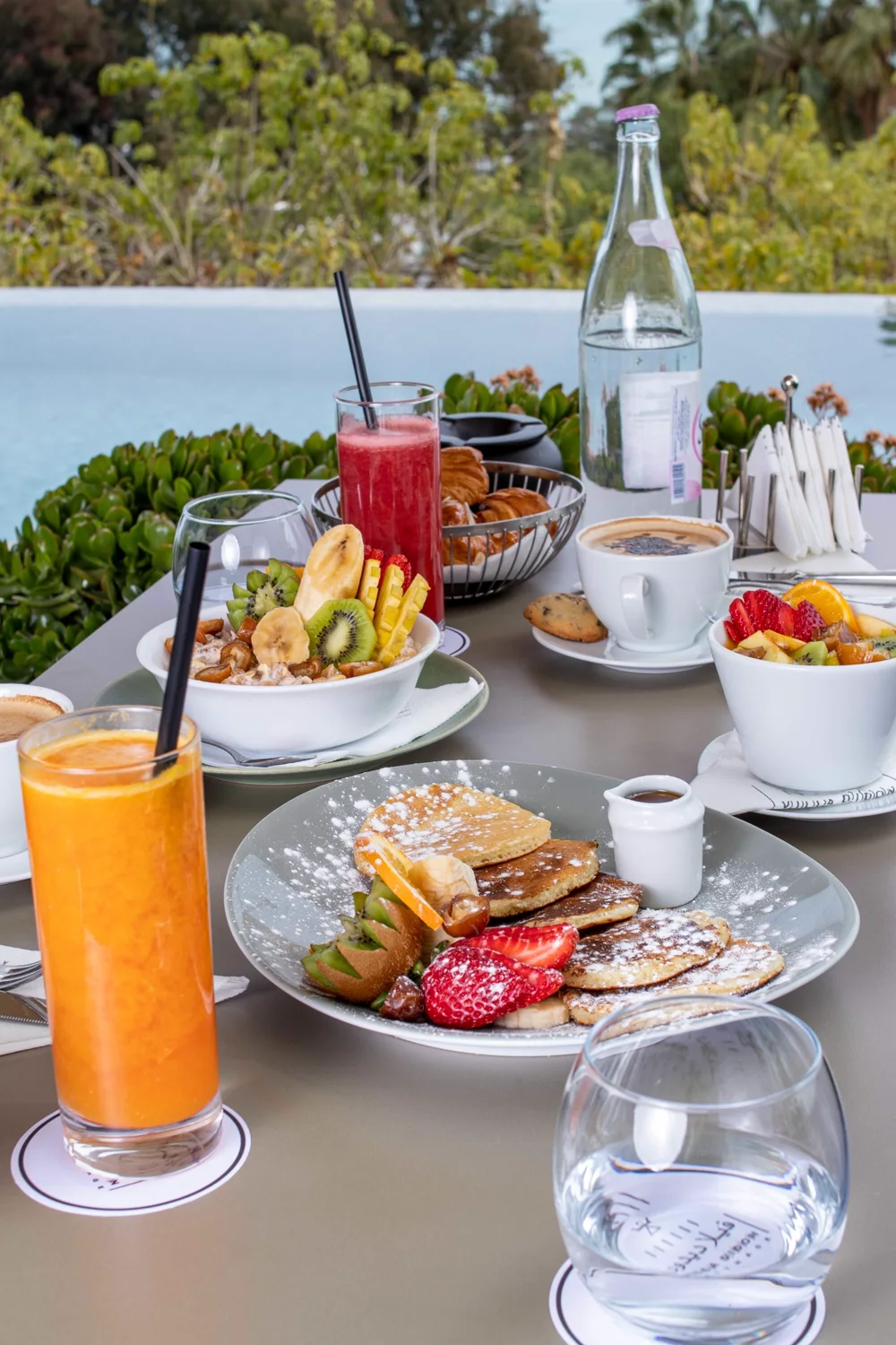 The full morning table — juices, coffees, fruit — facing the bay