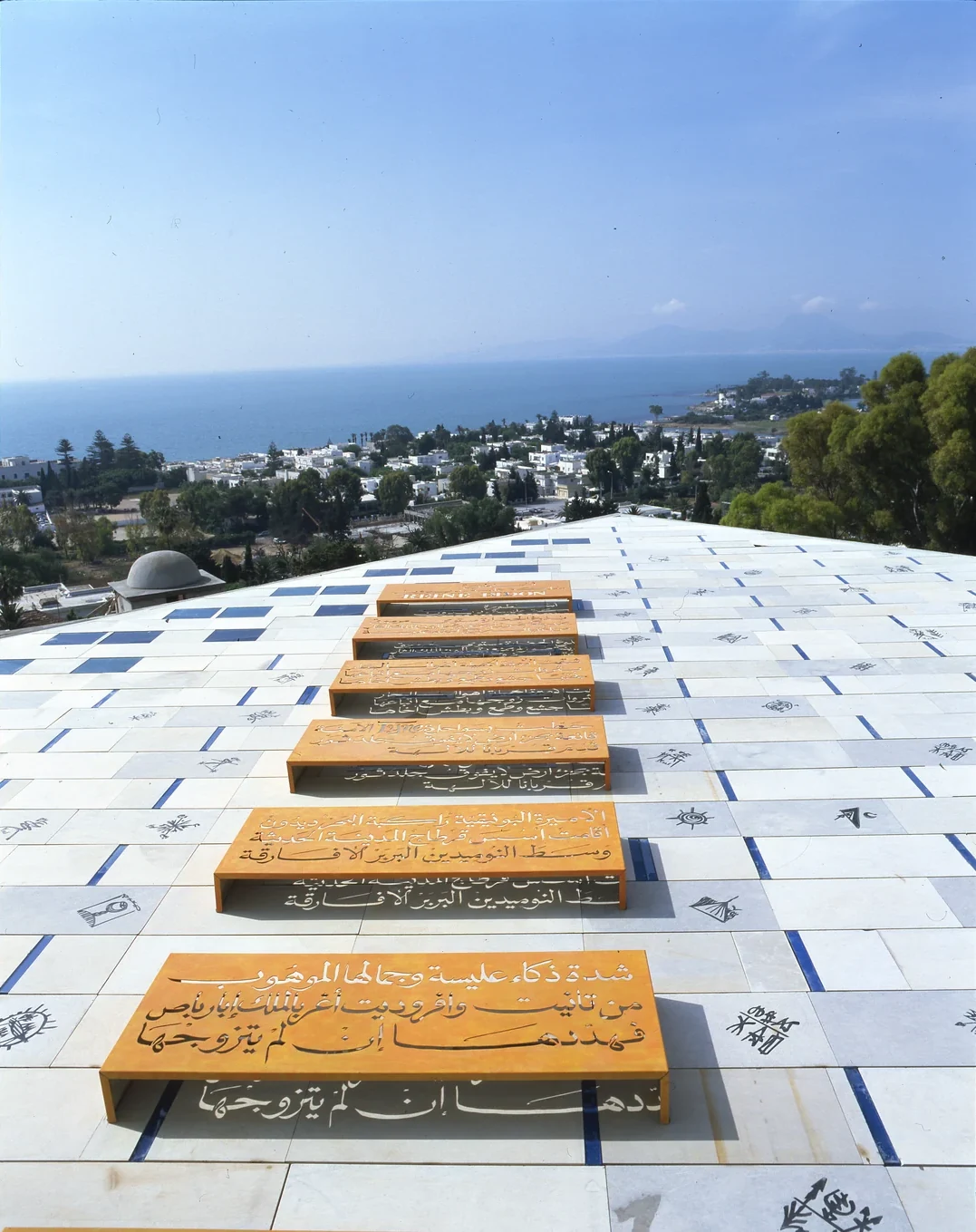 Rachid Koraïchi's calligraphed stelae lined along the villa's upper terrace, facing the bay of Carthage in broad daylight