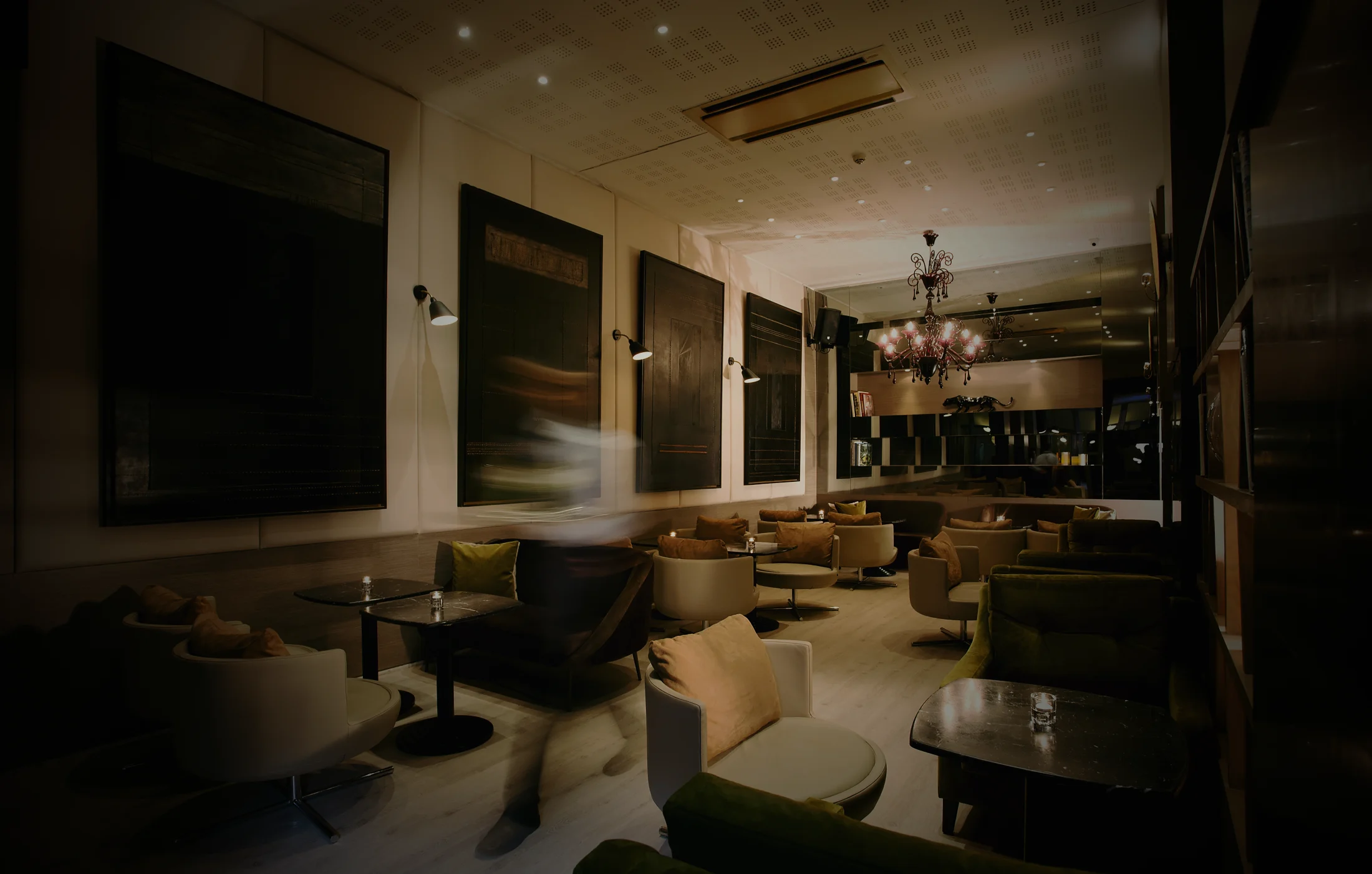 Le Light Bar in the half-light: armchairs and banquettes around small candlelit tables, the Venetian chandelier glowing at the far end