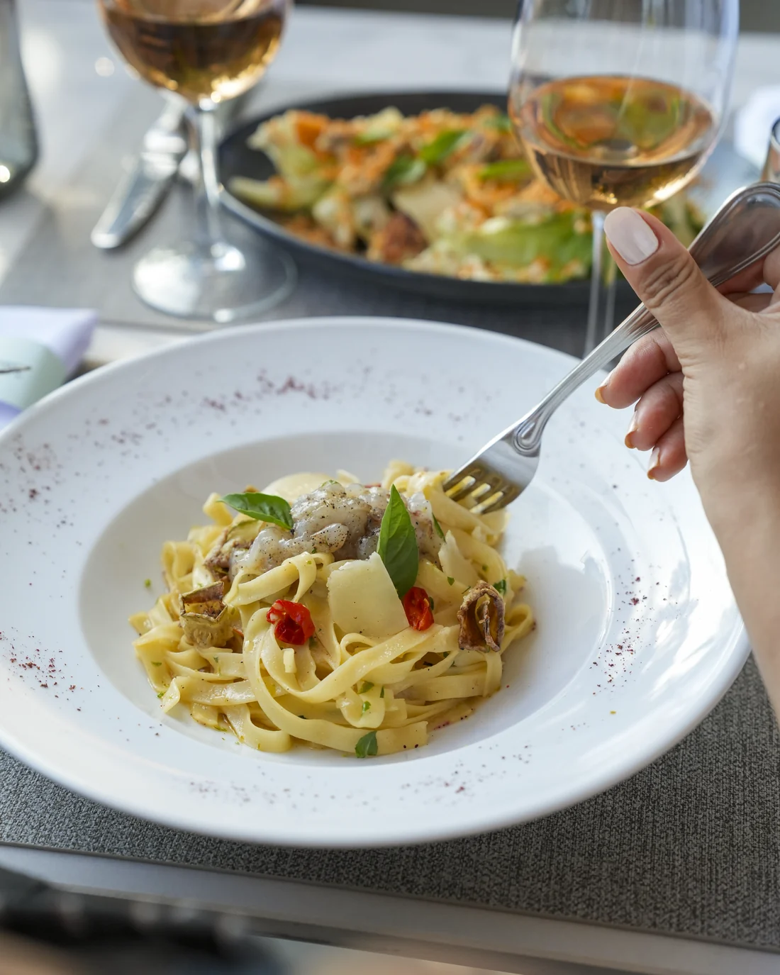 Lemon tagliatelle with garlic cream, courgettes and prawn tartare, basil, in a white plate, a glass of white wine beside it