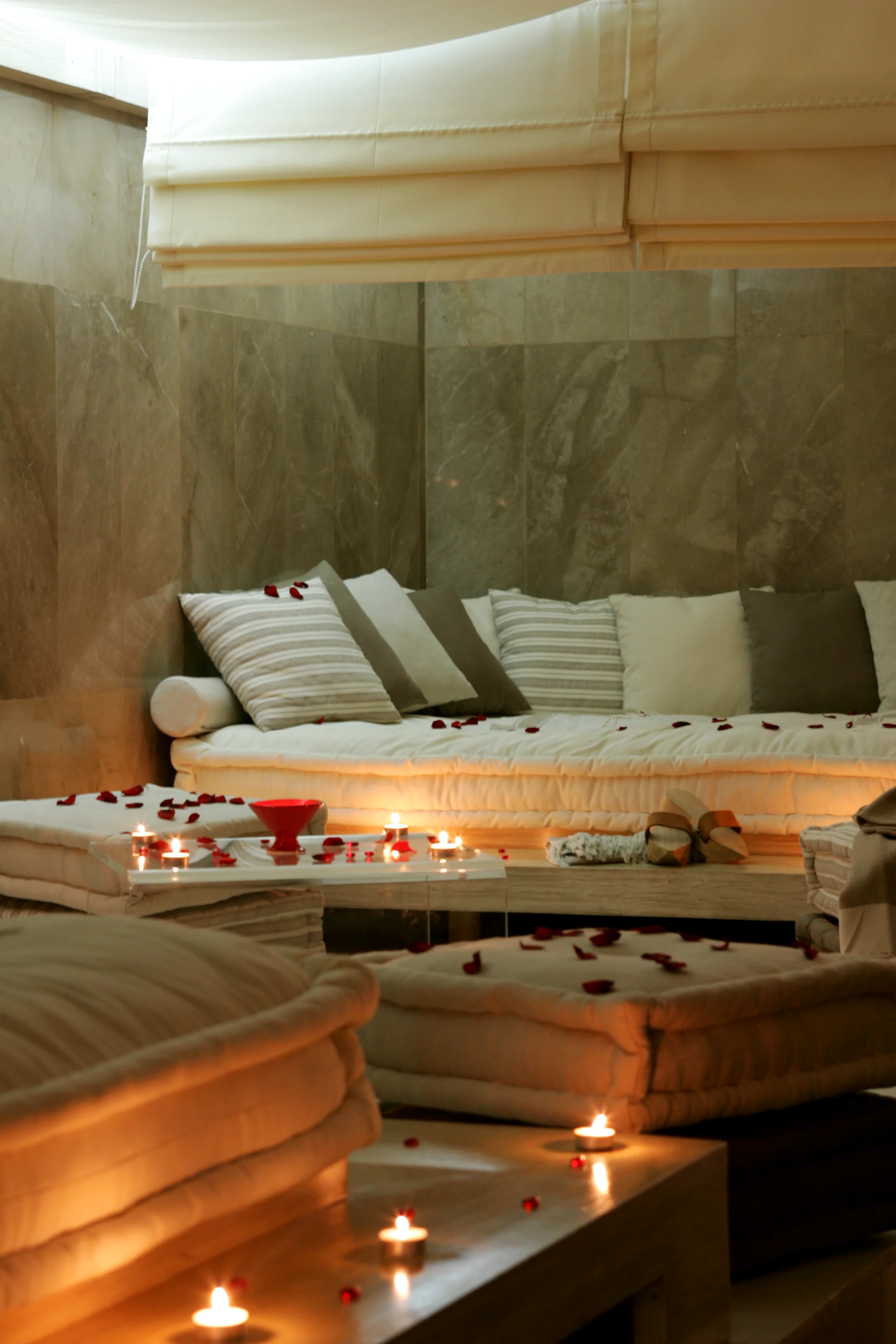 A daybed in the spa: striped cushions, pale backlit linen, rose petals and candles arranged around it